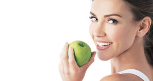 Woman with dental veneers holds granny smith apple